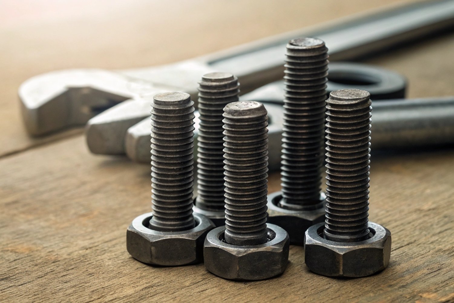 Close-up of industrial steel bolts and nuts on a rustic wooden workbench with tools.